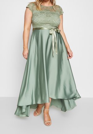 Groen kanten topjurkje met een satijnen rok, voorzien van een gestrikte lint in de taille en een asymmetrische zoom. Getextureerd kant en gladde stof.