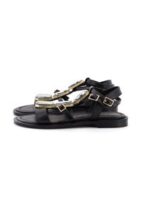 Sandali in pelle nera con un design a strisce, dettagli con fibbia dorata e elementi decorativi ovali sulla parte anteriore. Suola piatta.
