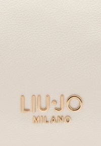 Cuir blanc texturé avec un logo doré en relief « LIU·JO MILANO » en bas, présentant une typographie moderne et élégante.