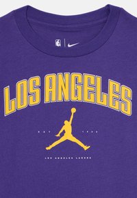 Lilla bomull T-skjorte med "LOS ANGELES" i fet gul skrift, en gul Jordan-silhuett, og teksten "EST 1960" under.