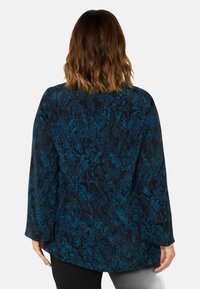 Modrá a černá vzorovaná halenka s dlouhým rukávem, která se vyznačuje volným střihem a splývavým designem. Tkanina má texturovaný vzhled s jemným leskem.