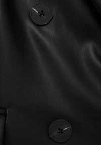 Tissu en cuir noir avec une texture lisse, présentant deux boutons ronds noirs à quatre trous, mettant en valeur la brillance et la douceur du matériau.