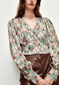 Blusa con motivo in verde pastello, caratterizzata da una scollatura a V, bottoni e maniche a sbuffo. Notevole per il suo design astratto multicolore e la texture morbida.