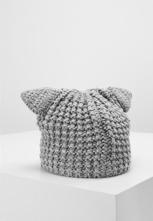 Bonnet en maille épaisse grise avec deux oreilles pointues, présenté sur un socle blanc sur un fond gris uni.