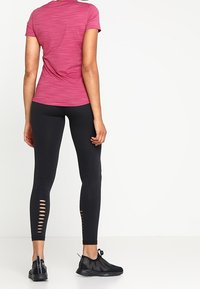 Figurvänlig rosa tränings T-shirt med en melerad struktur, kombinerad med svarta leggings som har sidokut och elastisk väv, bärs med svarta skor.