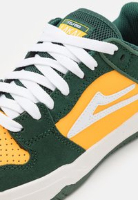 Sport sneaker with green suede, yellow panels, white logo, and white laces, labeled "Telford Lakai" on the tongue.