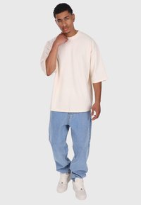 Overdimensioneret cremefarvet t-shirt lavet af blødt stof, parret med lyseblå løstsiddende jeans og hvide sneakers. Bemærkelsesværdige funktioner inkluderer korte ærmer.