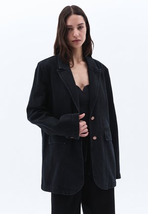 Černý oversized blazer z denimu s klopami, dvěma předními kapsami a měděnými knoflíky. Má hladkou texturu a proužkovaný detail.