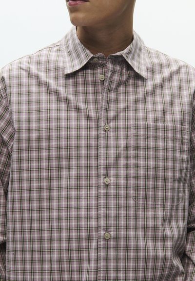 Camisa ligera de cuadros en tonos morado y verde, con cuello abierto, cierre de botones y un solo bolsillo en el pecho.