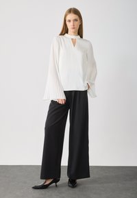 White blouse with pleated long sleeves and a keyhole neckline, paired with wide-leg black trousers and black patent heels.