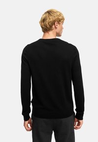 Pull en maille noir avec un col rond, des manches longues et des poignets et un ourlet côtelés. Texture lisse, design minimal, sans motifs ni accent visibles.