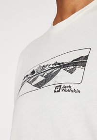 Witte katoenen T-shirt met een zwart graphic van gestileerde bergen en strepen; inclusief "Jack Wolfskin" logo. Korte mouwen met een ronde hals.