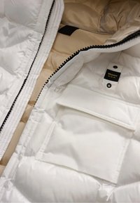 Interno di giacca a vento bianca con fodera beige, texture trapuntata, chiusura a zip e tasca esterna. Etichetta con "Blauer: U.S.A."