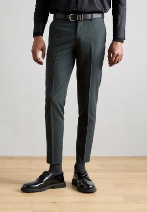 Pantaloni verdi su misura con vestibilità slim, caratterizzati da una trama liscia e pieghe ben stirate. Abbinati a scarpe in pelle nere e una cintura testurizzata.