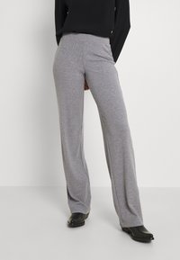 Šedé široké kalhoty z měkké látky s plochým pasem a volným střihem, doplněné černými botami.