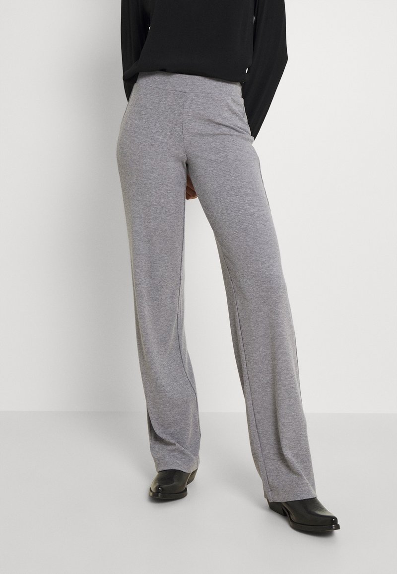 Šedé široké kalhoty z měkké látky s plochým pasem a volným střihem, doplněné černými botami.