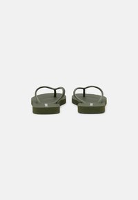 Grønne flip-flops med teksturert fotseng, tynne stropper og flate såler. Designet har enkle linjer og en minimalistisk stil.