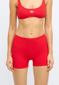 Κόκκινο σπορ μπικίνι τοπ και σορτς κατασκευασμένα από μαλακό, ελαστικό ύφασμα. Περιλαμβάνει τετράγωνο ντεκολτέ και διακοσμητική ραφή.