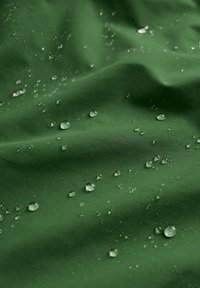 Wodoodporna zielona tkanina o gładkiej fakturze, z rozproszonymi kroplami wody odbijającymi światło na powierzchni.