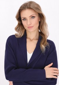 Cardigan navy con colletto a scialle e maniche lunghe, caratterizzato da una texture morbida e una vestibilità rilassata, indossato sopra una maglietta bianca a scollo a V.