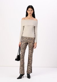 Off-shoulder beige ribbed sweater paired with leopard print flared pants. Model holds a black handbag; wearing black heeled boots.