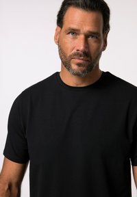 Černé tričko s krátkým rukávem a kulatým výstřihem vyrobené z bavlny. Látka působí měkce a hladce, těsně obepíná ramena a hruď.