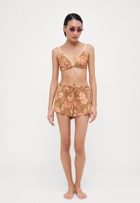 Bikini floral marron avec un haut triangulaire et un short assorti. Présente des accents pêche clair et un tissu texturé. Lunettes de soleil en rose pâle.