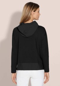 Zwarte, capuchonpullover met een cropped ontwerp; heeft lange mouwen en een contrasterende textuur aan de onderrand. Minimalistische stijl.