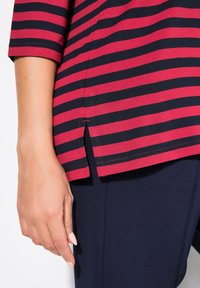 Rood en marineblauw gestreept top met een gespleten zoom en korte mouwen, gemaakt van een zachte stof. Gestructureerde afwerking met contrasterende stiksels.