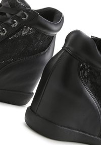 Schwarze Wedge-Sneaker zeichnen sich durch eine Kombination aus glattem Leder und strukturierten Schnüseelementen aus, mit einer abgerundeten Zehenpartie und einer Schnürung auf der Vorderseite.