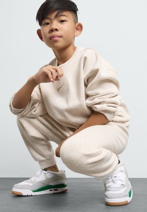 Beige Nike-Sweatshirt und -Sweatpants, kombiniert mit weißen Sneakers mit grünen Akzenten und einer Gummisohle, vor einem neutralen Hintergrund.
