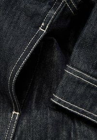 Κοντινή λήψη σκούρου τζιν υφάσματος που δείχνει λεπτομερή άσπρα ράμματα κατά μήκος τσέπης και άκρων ραφών.