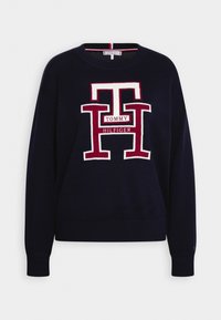 Pull en maille bleu marine avec un grand logo Tommy Hilfiger rouge et blanc centré sur le devant, avec des manches longues et des poignets et un ourlet côtelés.