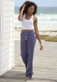 Witte cropped tanktop en loszittende paarse joggingbroek met drawstring, voorzien van zijzakken en subtiele logo borduursels.