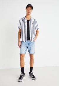 Svītrainā īsām piedurknēm krekls baltā un zilā krāsā, melns topiņš, gaiši džinsu šorti ar sarullētām malām, melni zeķes un jauktu materiālu sporta apavi.