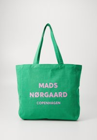 Sac fourre-tout en toile verte avec deux anses. Présente un texte rose vif : "MADS NØRGAARD COPENHAGUE" affiché de manière proéminente. Design simple.