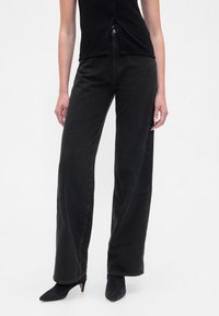 Čierne široké nohavice z denimu s vysokým pásom, vybavené zapínaním na gombíky a voľným strihom, doplnené o čierne špicaté lodičky.