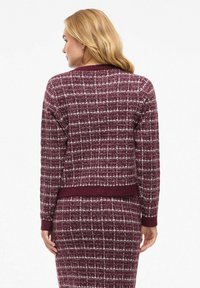 Cardigan bordeaux à motif avec un tissage texturé, présentant un ourlet et des poignets côtelés, vu de dos, assorti à une jupe correspondante.