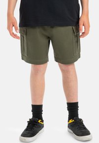 Olivgröna cargo-shorts med två sido-fickor, uppvikta fållar och ett slitstarkt bomullstyg. Matchas med svarta strumpor och skor.