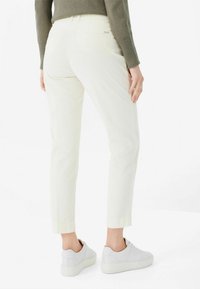 Weiße Cordhosen mit Slim-Fit, ausgestattet mit einer normalen Taille und einem knöchellangen Schnitt, kombiniert mit hellgrauen Sneakers.