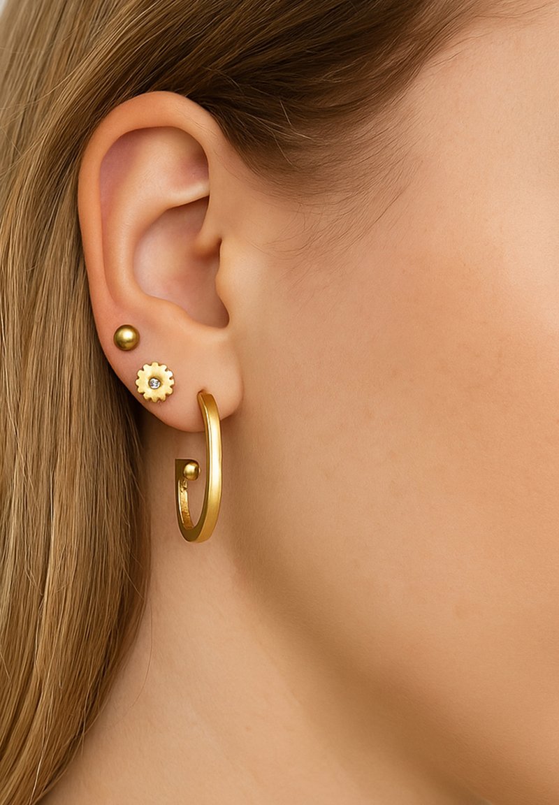 Goldene Creole mit offenem Design, kombiniert mit einem runden goldenen Stecker und einem blumenförmigen Stecker mit einem klaren Edelstein, im Ohr getragen.