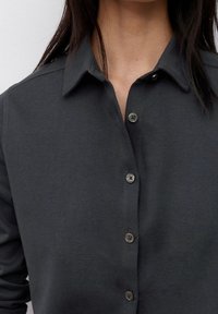 Camicia button-up grigia scura realizzata in tessuto morbido, con colletto classico, bottoni visibili e una texture liscia.