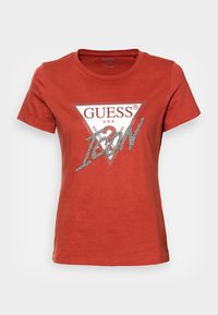 Camiseta de mujer de manga corta en color óxido con el logo triangular de GUESS y el texto "ICON" en brillantes plateados en la parte frontal.