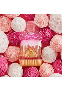 Butelka perfum z różową kokardą, białymi kroplami i złotym emblematem, otoczona różowo-białymi, skręconymi babeczkami z perełkowymi ozdobami.