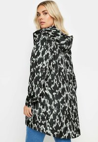 Svartvit mönstrad regnjacka med huva, i ett lätt, glänsande material och med dragsko i midjan för en skräddarsydd passform.