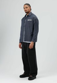 Blauw geruit overhemd met een borstzak, knoopsluiting en geborduurde tekst. Zwarte wijde jeans en zwarte schoenen met een dikke zool.