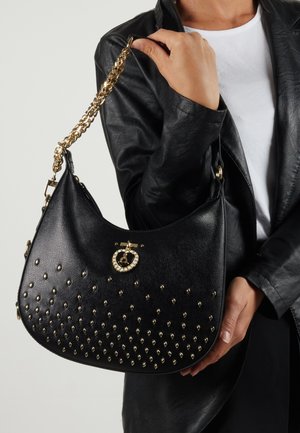 Borsa a tracolla in pelle nera con dettagli borchiati sul davanti, tracolla in catena dorata e un accento di hardware metallico rotondo sulla parte superiore.