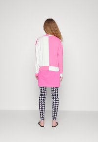 Långärmad topp i rosa och vit färgblockdesign, tillsammans med leggings med svartvitt hjärt-mönster och platta sandaler.