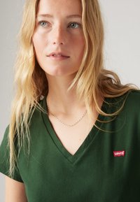 Green v-neck t-shirt made of soft fabric, featuring short sleeves and a small red Levi's logo on the left side.