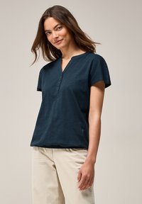 Top corto a maniche corte di colore blu navy con colletto a fascetta, chiusura con bottoni e una vestibilità leggermente ampia. Realizzato in un tessuto leggero e testurizzato.